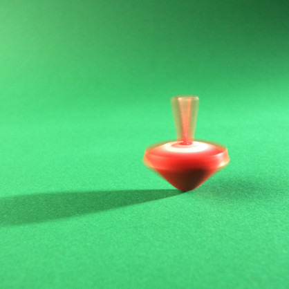 Bewegungsambulatorium Ein sich drehender, roter Kreisel auf einem grünen Untergrund, mitten in der Bewegung eingefangen.